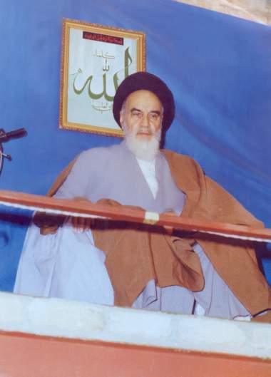 Imam Khomeini discursando e atrás dele um quadro com apalavra Allah (Deus)